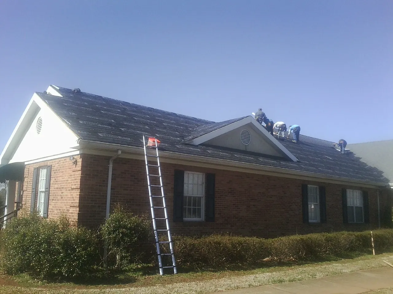 Crew tearing shingles off a brick ranch roof with a ladder set — Emergency Roof Repair work by our crew in Jaffrey