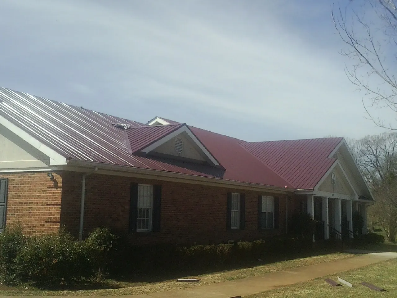 Red metal roof with gabled entries on a long brick building, from a Hail Damage Roof Repair job in Jaffrey