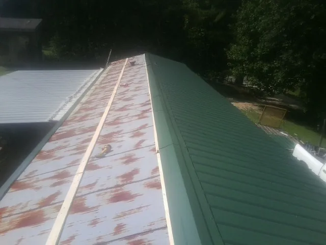 Old rusted panels beside newly installed green metal roofing — Wind Damage Roof Repair by Roofing Brothers in Jaffrey