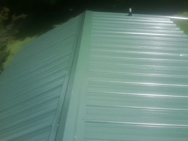 New green metal panels meeting at the ridge of a roof — Flat Roof Repair work by our crew in Jaffrey