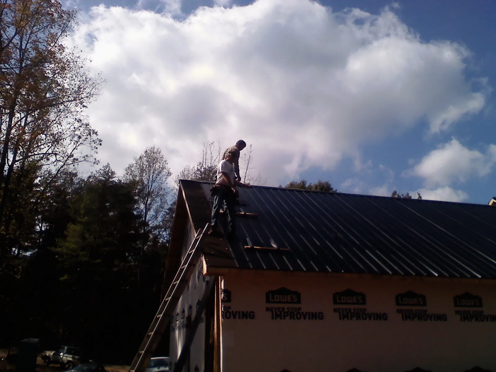 Roofer fastening dark metal panels high against a cloudy sky, from a Roof Inspection job in Jaffrey