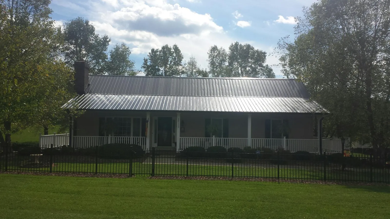 Gray metal roof on a brick ranch with a full width front porch — Gutter Guard Installation work by our crew in Jaffrey