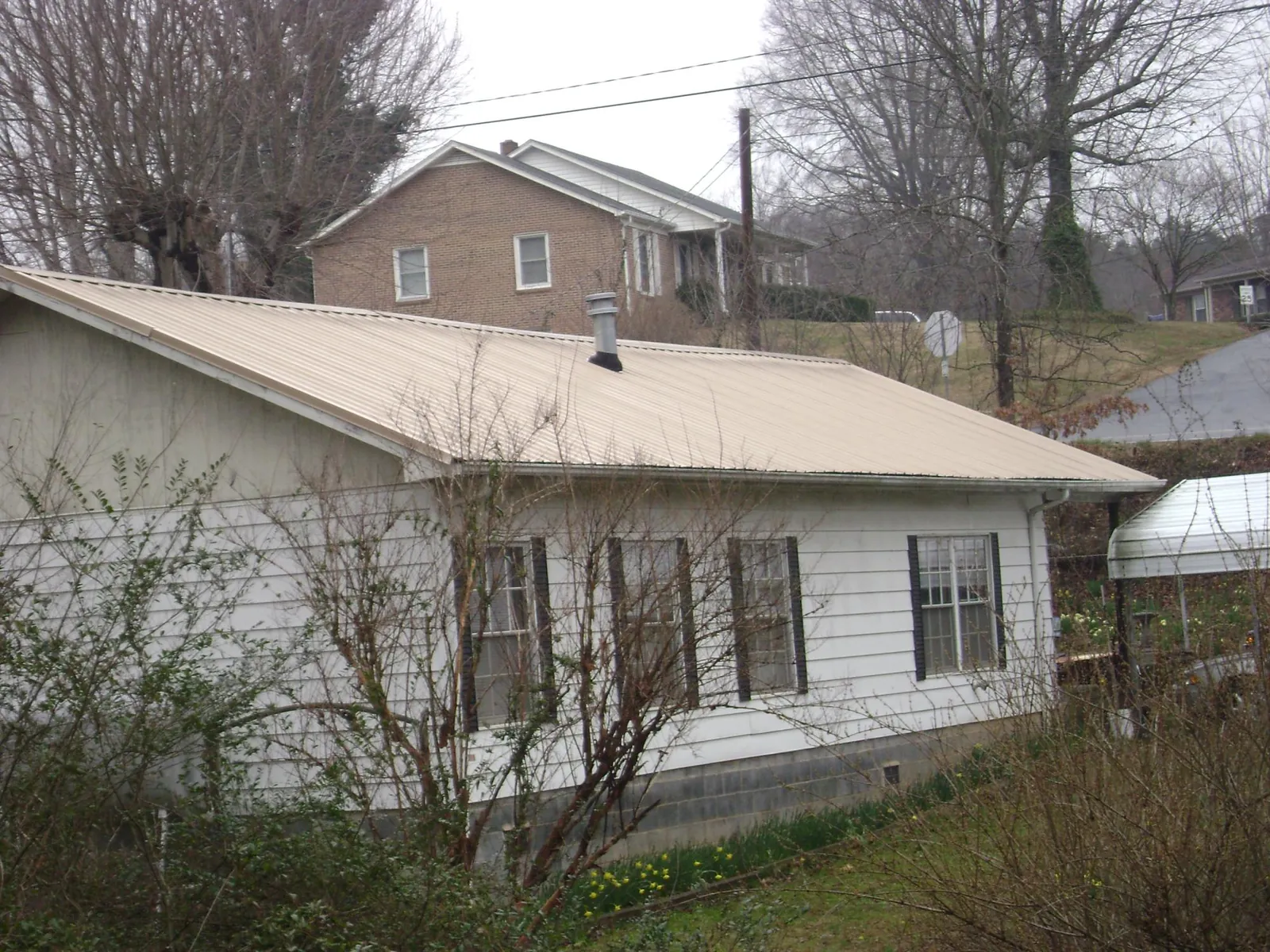Tan metal roof on a white sided house set into a hillside — Commercial Roofing by Roofing Brothers in Jaffrey