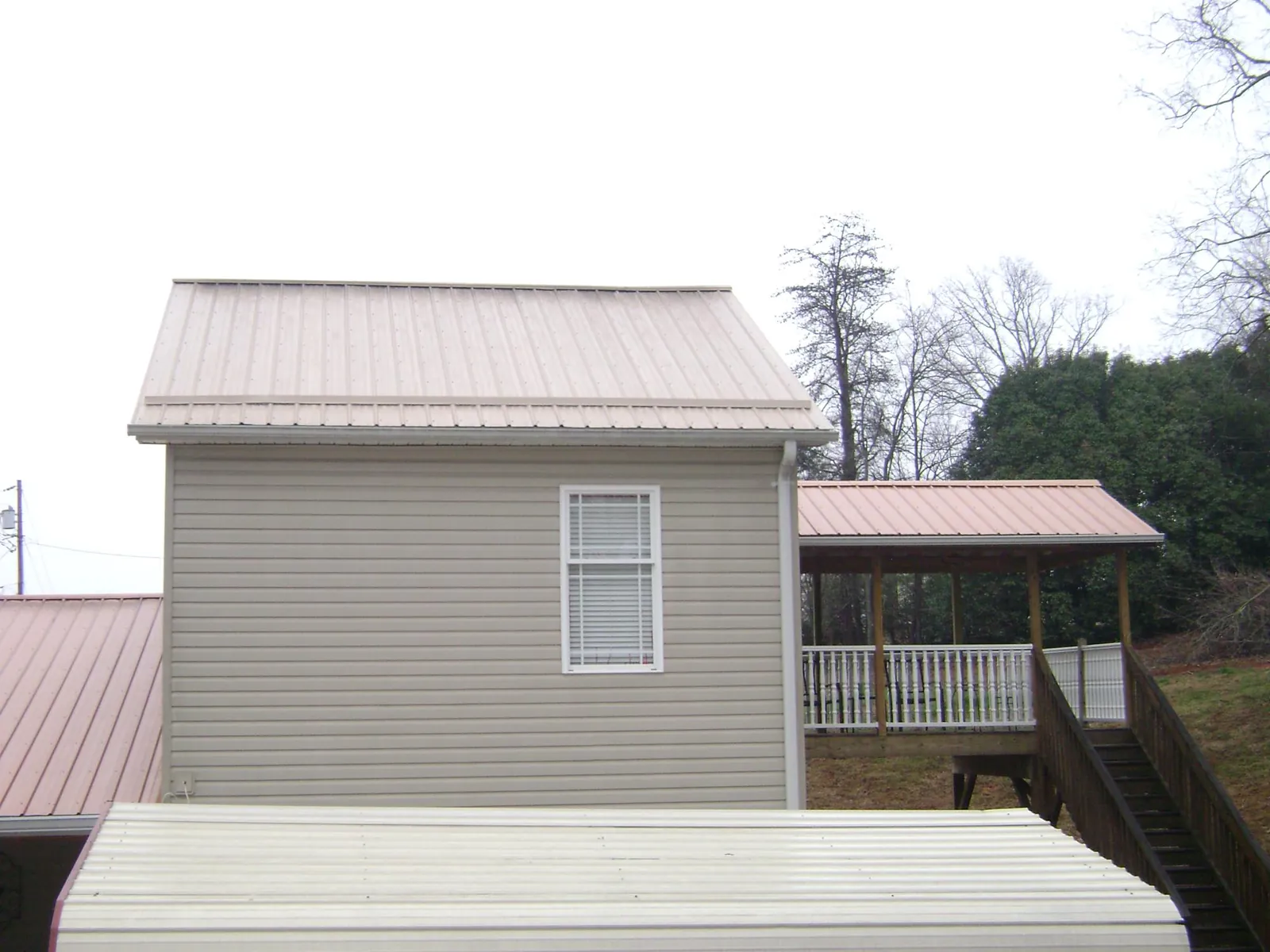 Tan metal roofs on a two story addition and attached porch, from a Roof Replacement job in Jaffrey